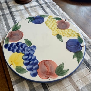 May include: A white ceramic serving platter with a blue rim, featuring a painted design of fruit, including grapes, apples, and plums. The fruit is painted in shades of red, yellow, blue, and green.