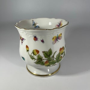 May include: A white porcelain cup with a gold rim and a floral design featuring strawberries, butterflies, and ladybugs.