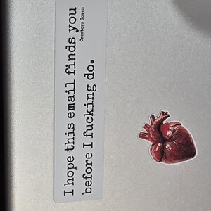 May include: A rectangular white sticker with black text that reads "I hope this email finds you before I fucking do." and "Creators Coven" in smaller font, accompanied by a separate sticker of a realistic, dark red anatomical human heart.