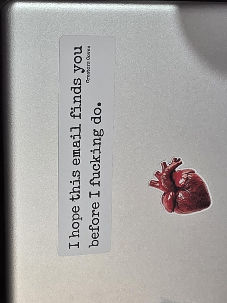 May include: A rectangular white sticker with black text that reads "I hope this email finds you before I fucking do." and "Creators Coven" in smaller font, accompanied by a separate sticker of a realistic, dark red anatomical human heart.