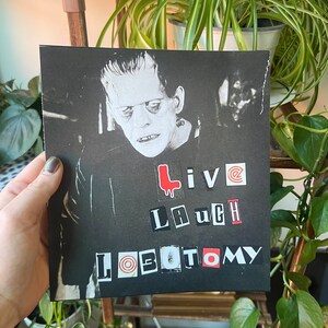 May include: Black and white image of Frankenstein's monster with the words "Live Laugh Lobotomy" in red and black letters.