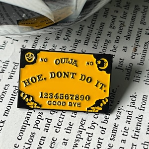 Könnte beinhalten: Gelb-schwarzer Email-Pin mit dem Text "HOE, DONT DO IT." und den Zahlen 1234567890 darunter. Der Text "GOOD BYE" befindet sich unter den Zahlen. Der Pin hat einen schwarzen Umriss und einen schwarzen Halbmond mit einem Stern oben rechts.