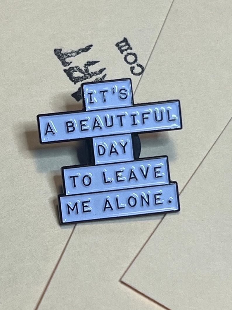"it's a beautiful day to leave me alone." this is a soft enamel pin that is white with blacks words.