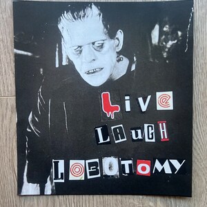 May include: Black and white image of a monster with the words "Live Laugh Lobotomy" in red and white letters.