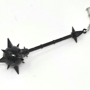 May include: A black mace keyring featuring a spiked ball head and a long handle. The keyring has a silver-coloured chain and clasp. The mace is a miniature replica of a medieval weapon.