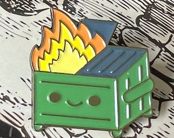 Può includere: Uno spillo di metallo verde a forma di bidone della spazzatura con un viso sorridente. Il bidone della spazzatura è in fiamme con fiamme arancioni e gialle.