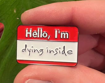 May include: Red and white enamel pin with the text "Hello, I'm dying inside" on a name tag.