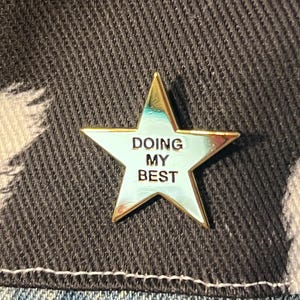 May include: Gold star-shaped pin with a light blue background and the text "DOING MY BEST" in black.