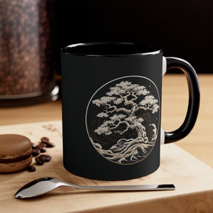 May include: Black ceramic mug with a white design of a stylized bonsai tree in a circle with waves and stars. The mug has a white interior and a black handle.