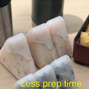 May include: Four white silicone food containers shaped like triangles. The containers are filled with white rice and other ingredients. The text "Less prep time" is visible at the bottom of the image.