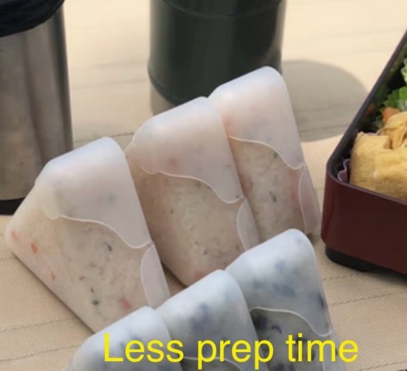 May include: Four white silicone food containers shaped like triangles. The containers are filled with white rice and other ingredients. The text "Less prep time" is visible at the bottom of the image.