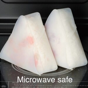 May include: Two white silicone food covers shaped like triangles. The covers are on a black surface and the text "Microwave safe" is printed below them.