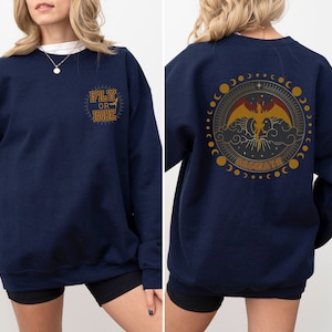 May include: Navy blue sweatshirt with gold text that says "FLY OR DIE" on the front. The back features a circular design with a dragon, clouds, and the word "BASMATH".
