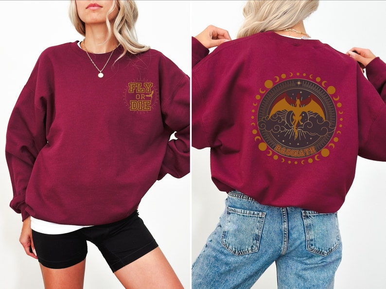 May include: Burgundy sweatshirt with "FLY OR DIE" text on the front and a circular graphic on the back featuring a dragon, clouds, and the word "BASGARTH". The design is in gold and brown tones.