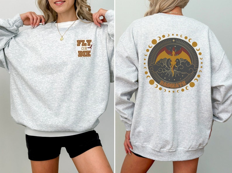May include: Light gray sweatshirt with the text "FLY OR DIE" on the front and a circular graphic on the back featuring a phoenix, clouds, and the word "BASGIATH". The design includes gold and brown accents.