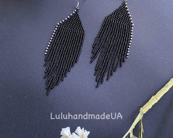 May include: A pair of black beaded fringe earrings with silver-colored accents. The earrings have a teardrop shape and are displayed on a dark background with white flowers. The text "LuluhandmadeUA" is visible.