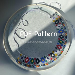 May include: A colourful beaded necklace with a geometric design, featuring red, blue, green, and yellow beads. The necklace is displayed on a grey plate. The text "PDF Pattern" and "LuluhandmadeUA" are visible.