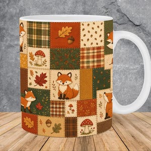 May include: A white ceramic mug featuring a patchwork design of autumn-themed squares. The pattern includes illustrations of orange foxes, red mushrooms, brown acorns, and various fall leaves in shades of orange, green, and tan, with plaid accents.
