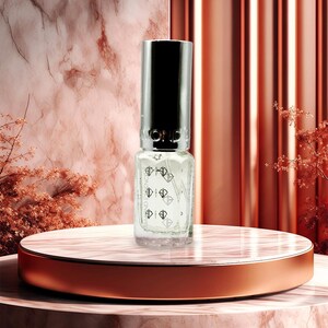 May include: A clear glass bottle of nail polish with a silver cap, featuring a diamond design. The bottle sits on a marble and copper-colored platform. The background includes a marble wall and a copper-colored, vertically-lined backdrop.
