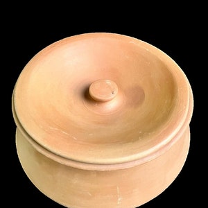 May include: A terracotta pot with a lid. The pot is a light brown color and has a smooth, rounded shape. The lid has a small knob on top.