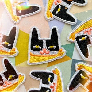 May include: A set of nine embroidered iron-on patches featuring black and white cats with yellow and white accents. The cats are wearing yellow and white bandanas.