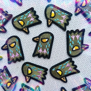 May include: A set of nine embroidered iron-on patches featuring a cartoon bird design. The patches are green, blue, and pink with black outlines.