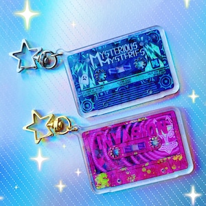 May include: Two colorful cassette tape keychains with gold metal rings. The blue keychain has the text "MYSTERIOUS MYSTERIES" and the pink keychain has the text "INVASION".