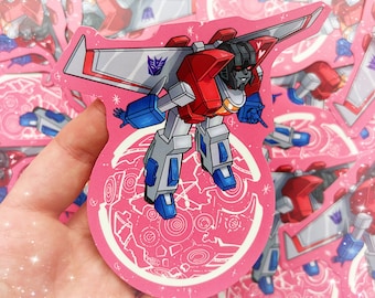May include: A pink and white sticker featuring a cartoon illustration of Starscream, a red and blue robot from the Transformers franchise, flying in space. The sticker has a white outline and a pink background with a white pattern.