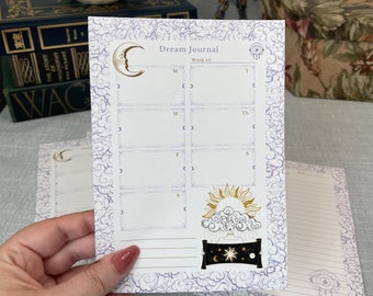 May include: A white dream journal with a purple and white floral pattern. The cover features a crescent moon, a sun, and a sleeping figure with a crown. The inside pages are lined and have a space for each day of the week to record dreams.