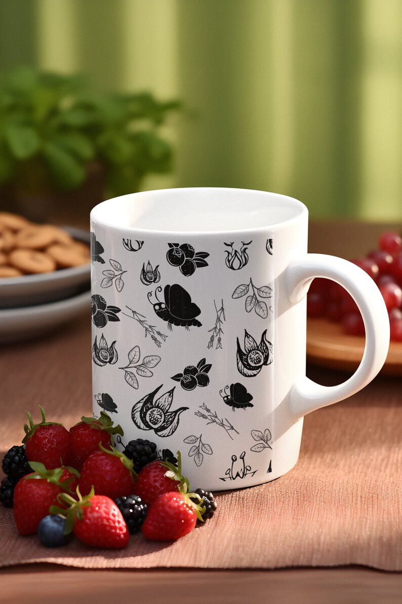 Puede incluir: Taza de cer&aacute;mica blanca con un patr&oacute;n bot&aacute;nico en blanco y negro con flores, hojas y mariposas. La taza est&aacute; llena de una bebida y est&aacute; rodeada de fresas y moras frescas. La taza tiene un asa curvada.