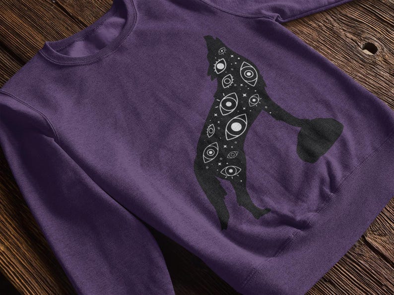 K&ouml;nnte beinhalten: Ein lila Sweatshirt mit einer schwarzen Silhouette eines heulenden Wolfes. Der Wolf ist mit wei&szlig;en Augen und Sternen gef&uuml;llt. Das Sweatshirt hat einen Rundhalsausschnitt und lange &Auml;rmel.