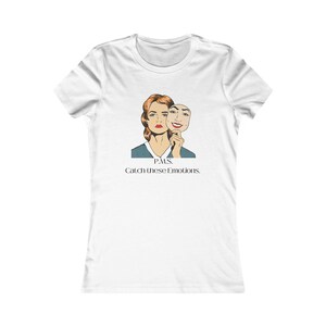 Könnte beinhalten: Weißes T-Shirt mit einem Grafikdruck einer Frau, die eine Maske hält, die zwei verschiedene Ausdrücke zeigt. Der Text "PMS. Catch these emotions." ist unter dem Grafikdruck aufgedruckt.