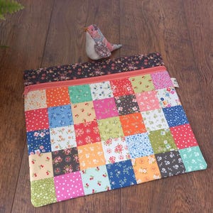 Può includere: Una pochette quadrata in tessuto con un design patchwork composto da vari motivi floreali e a pois colorati nelle tonalità del rosso, blu, verde, arancione e rosa. La pochette presenta una cerniera color corallo e un bordo in tessuto floreale scuro.