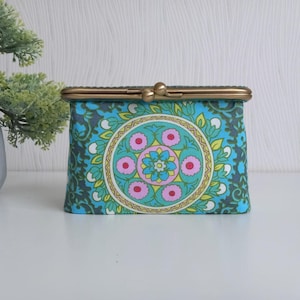 May include: A blue and green patterned coin purse with a gold metal clasp. The pattern features a large circular design with pink and yellow flowers.