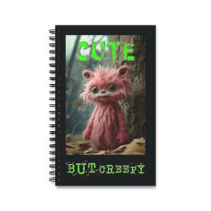 May include: A black spiral notebook with a pink furry creature with big eyes on the cover. The creature is standing in a forest setting. The text "CUTE BUT CREEPY" is written in green letters on the cover.