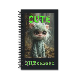 May include: A black spiral notebook with a green and white image of a furry creature with large eyes. The text "CUTE BUT CREEPY" is printed in green on the front of the notebook.