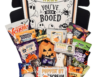 May include: A black gift box filled with assorted Halloween-themed snacks and treats. The box lid features the text "YOU'VE BEEN BOOED" with ghost and spider illustrations. Included items have labels reading "SPOOKY VIBES," "S'MORE SPOOKY SWEETS," and "POPPIN' BY TO SCREAM BOO."