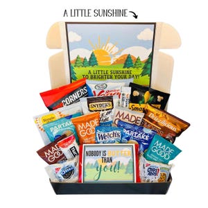 May include: A gift box filled with various snack-sized treats, including chips, cookies, and popcorn. The box features a scenic illustration with the text "A Little Sunshine to Brighten Your Day!" and "Nobody is Butter Than You!"