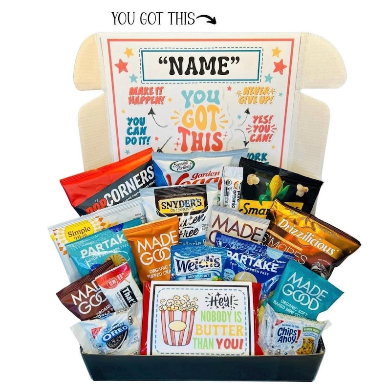 May include: A gift box filled with various snacks, including popcorn, chips, and cookies. The box has a personalized label with the text "NAME" and motivational phrases like "You Got This!" and "Make it Happen!"