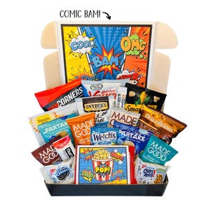 May include: A gift basket filled with various snacks, including chips, cookies, popcorn, and candy. The box features a comic book theme with bold colors and text like "COOL," "BAM," and "POP!" The snacks are arranged in a black tray.