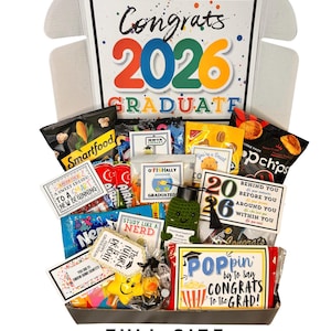 May include: A graduation gift box filled with snacks, candy, and small gifts. The box features a large sign that says "Congrats 2026 Graduate." The box includes bags of chips, candy, and a small crocheted graduation cap.