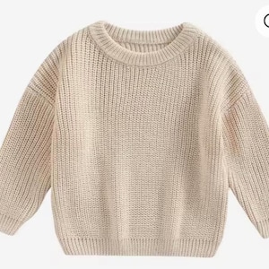 May include: A beige, chunky knit sweater with a crew neck and long sleeves. The sweater has a ribbed hem and cuffs. The knitwear is a neutral color, suitable for various outfits. This cozy sweater is perfect for cooler weather.