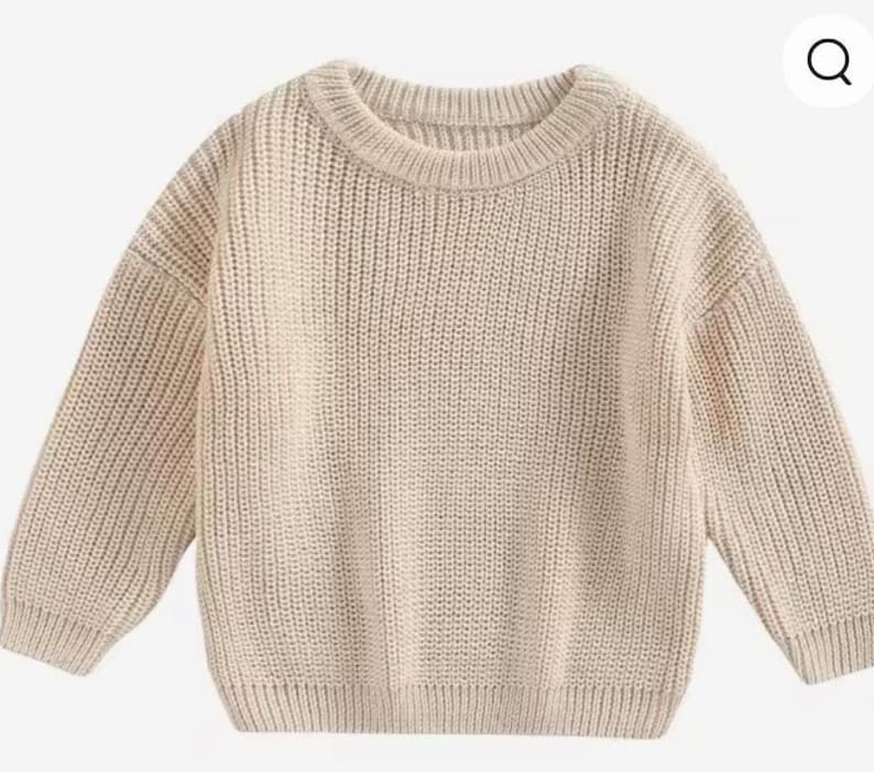May include: A beige, chunky knit sweater with a crew neck and long sleeves. The sweater has a ribbed hem and cuffs. The knitwear is a neutral color, suitable for various outfits. This cozy sweater is perfect for cooler weather.