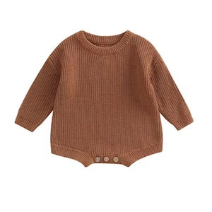 May include: A brown knit baby romper with long sleeves and a round neckline. The romper has a ribbed texture and three small buttons at the bottom. The garment is made of a soft, warm material.