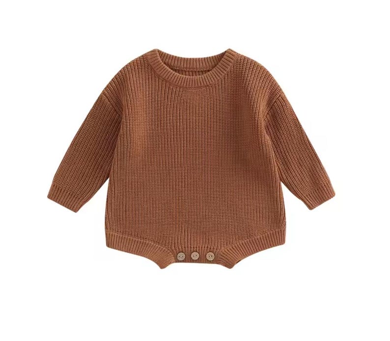 May include: A brown knit baby romper with long sleeves and a round neckline. The romper has a ribbed texture and three small buttons at the bottom. The garment is made of a soft, warm material.