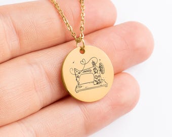 May include: Gold-colored necklace with a round pendant featuring a detailed black illustration of a vintage sewing machine. The pendant is suspended from a delicate chain, creating a charming accessory for sewing enthusiasts.
