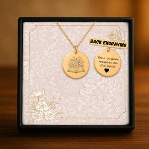 May include: A gold-colored necklace with two round pendants. One pendant features a floral design over an open book, the other has the text "Your custom message on the back" with a heart. The necklace is displayed in a decorative box.