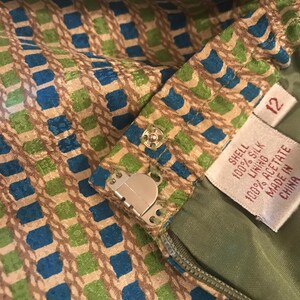 May include: A green and blue patterned skirt with a zipper and a metal hook and eye closure. The skirt has a label that reads "Shell 100% Silk Lining 100% Acetate Made in China" and a size tag that reads "12".