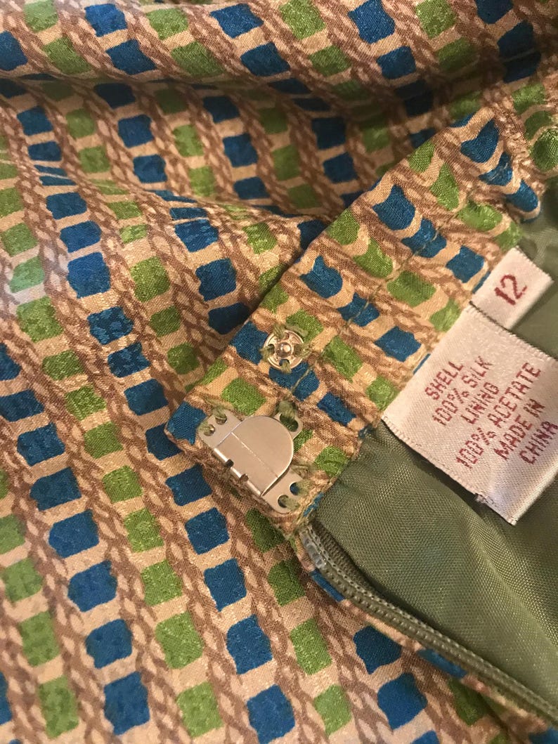May include: A green and blue patterned skirt with a zipper and a metal hook and eye closure. The skirt has a label that reads "Shell 100% Silk Lining 100% Acetate Made in China" and a size tag that reads "12".
