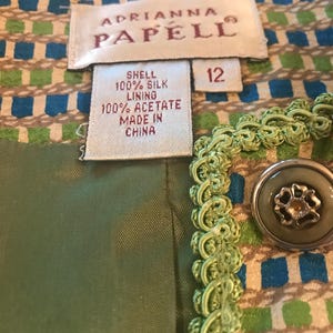 May include: A green and brown patterned fabric with a green trim and a green button. The fabric has a label that reads "Adrianna Papell" and "Shell 100% Silk Lining 100% Acetate Made in China" and a size tag that reads "12".
